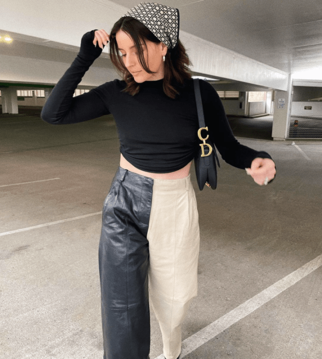 chica de cabello castaño usando un crop top negro de manga larga, pantalones de cuero negro con beige, bolso negro pequeño