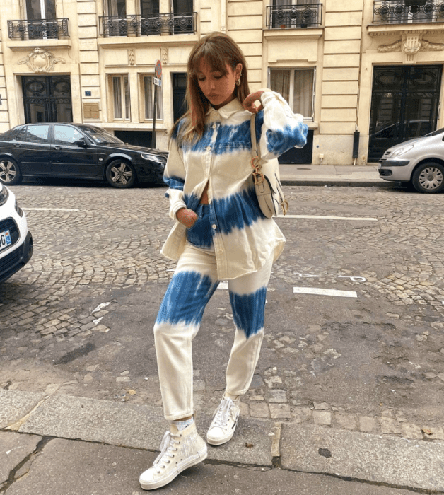 chica de cabello claro usando una camisa de mezclilla azul con rayas horizontales beige, pantalones holgados azules con líneas horizontales beige, tenis blancos 