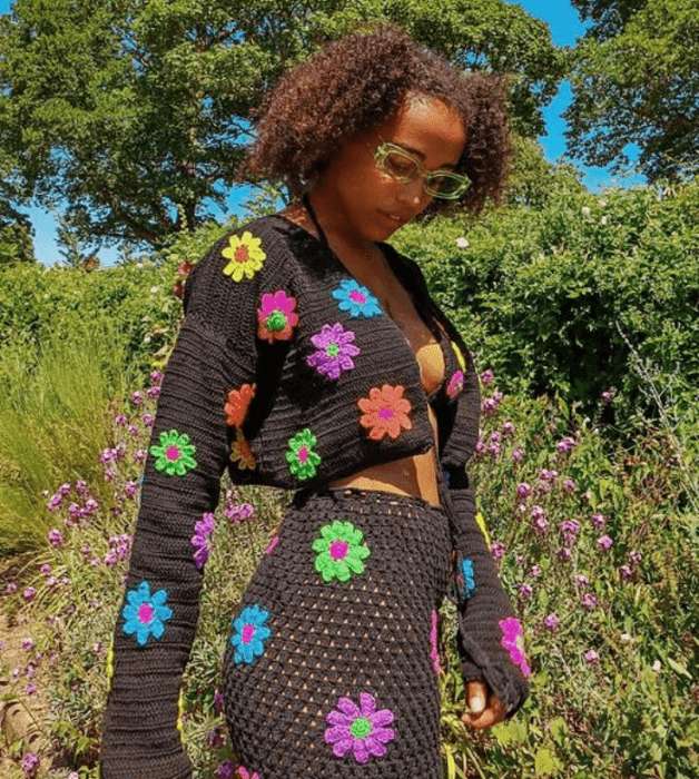 chica morena con cárdigan negro tejido con flores amarillas, verdes, moradas, azules, naranjas, minifalda negra tejida con flores de colores, bralette negro con flores