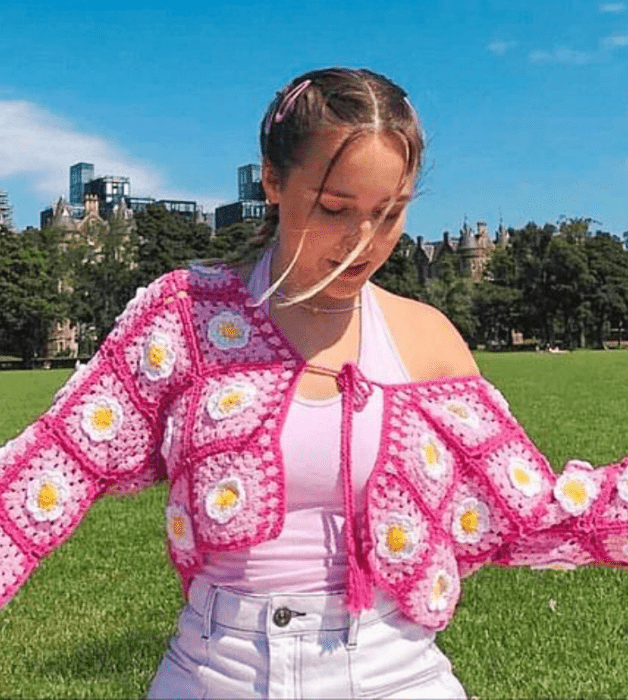 chica de cabello claro usando un top blanco de tirantes, cárdigan rosa fucsia con flores rosas y amarillas, jeans blancos ajustados