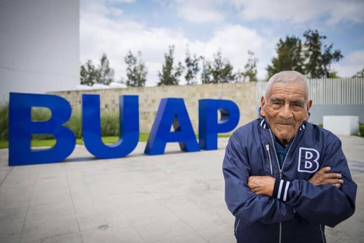 Abuelito de 84 años que se graduó de Ingeniero posando frente a la universidad 