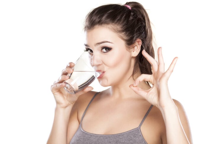 Chica tomando agua mientras hace una señal con las manos 