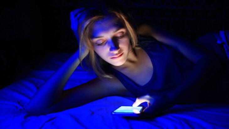 chica sosteniendo un celular con luz azul en sus manos