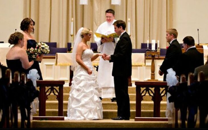 Pareja de novios frente al altar poniéndose los anillos 