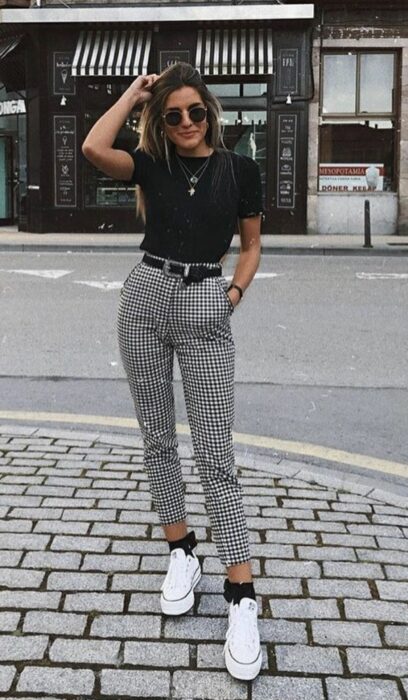 Chica usando pantalón de cuadros con blusa negra y tenis blancos