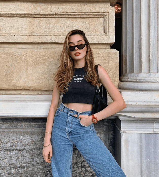 chica de cabello largo usando un crop top blanco, negro,. beige, café, verde, azul de manga larga, corta, con jeans ajustados, pantalones negros de cuero, bolso pequeño de mano