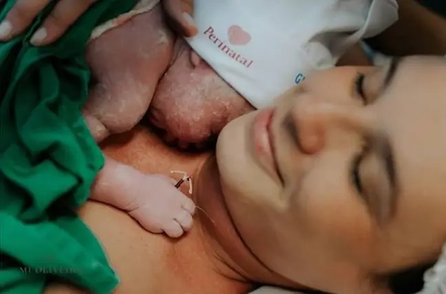 Mamá sosteniendo a su bebé en el pecho mientras él trae un Diu en la manita 