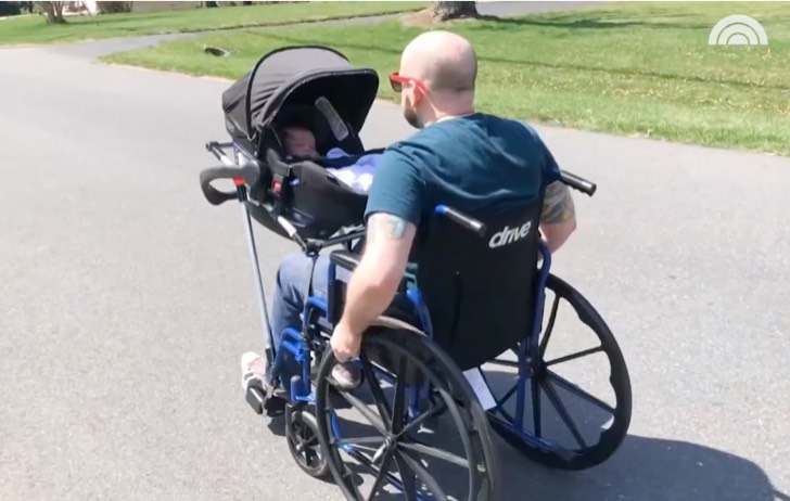 Man in a wheelchair walking his baby in a baby carrier 