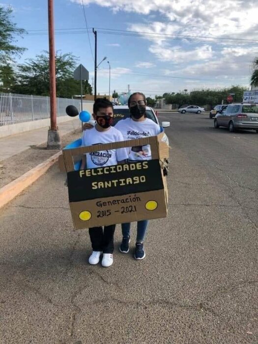 Mujer junto a su hijo dentro de un auto de cartón caminando por una caravana de autos 