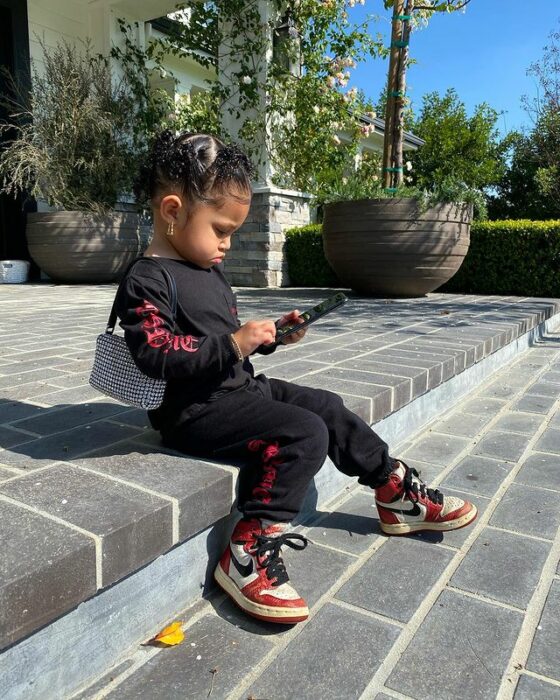 Stormi viendo su telefono mientras está sentada en las escaleras de su casa 