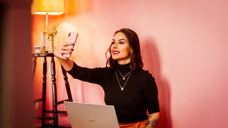 Chica tomando selfie frente a una computadora ;Nueva ley determina que las influencers deberán declarar si retocaron sus fotos o no