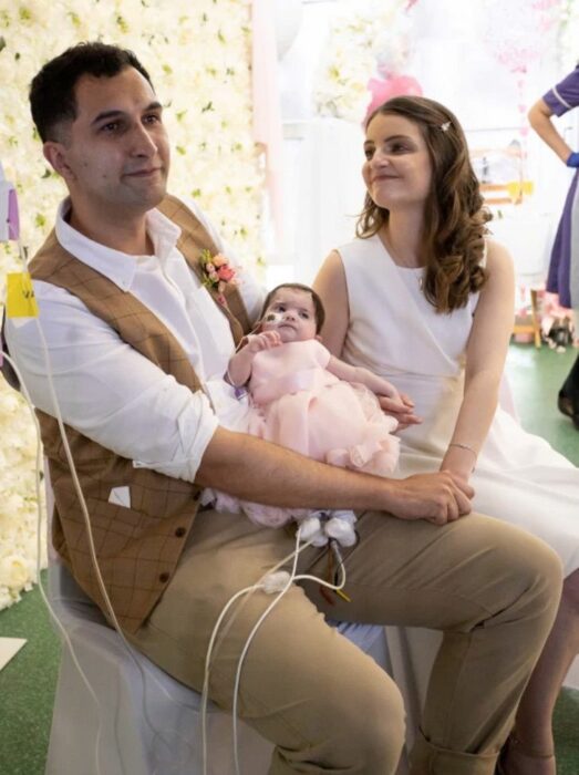 Couple holding their baby on their wedding day 