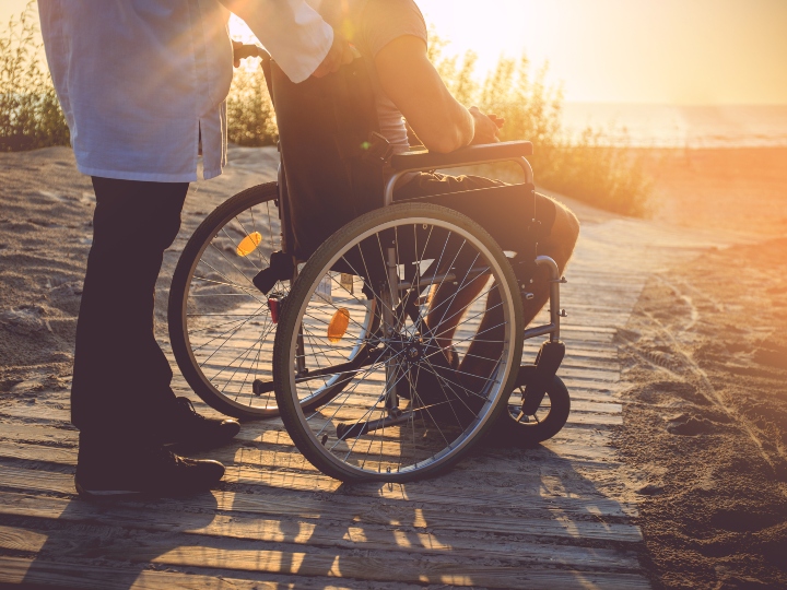 Son paves the way in the sand for his mother in a wheelchair to reach the seashore