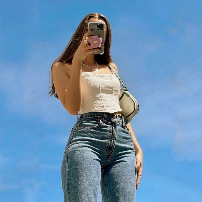 chica posando de manera original, con flores, en un campo abierto, frente a un espejo, con ropa trendy, jeans, falda, outfit lindo, botas, manicure, uñas postizas, lentes de sol