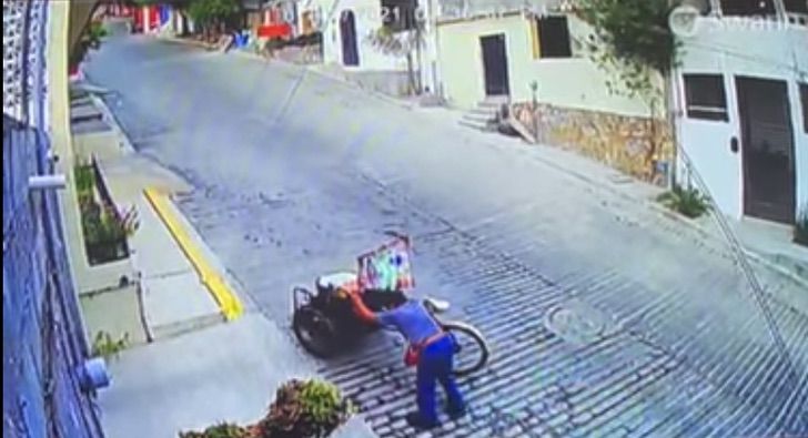 Hombre subiendo una colina empinada mientras sujeta su triciclo 