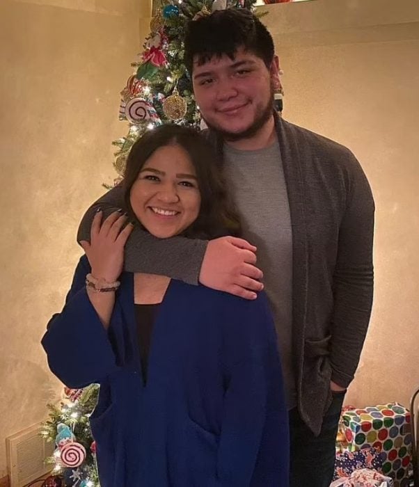 Chica abrazando a su novio mientras están frente al árbol de Navidad 
