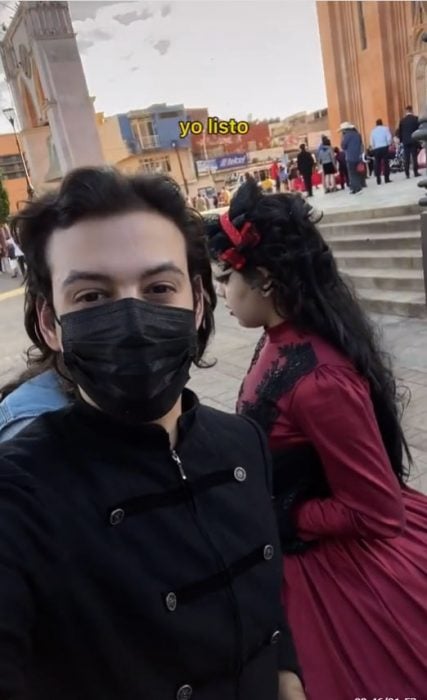 selfie de un chico con cubreboca negro junto a una chica con vestido negro con rojo 