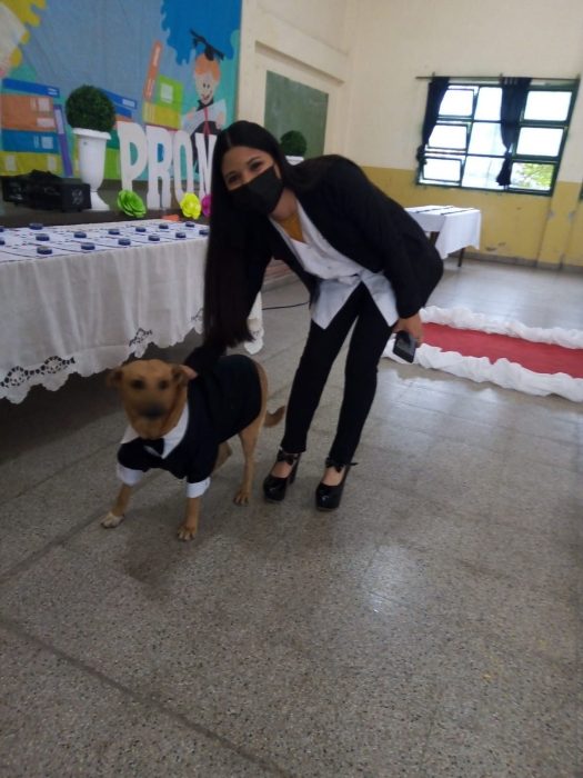 mujer posando a lado de un perro con traje negro en la ceremonia de una escuela en Argentina 