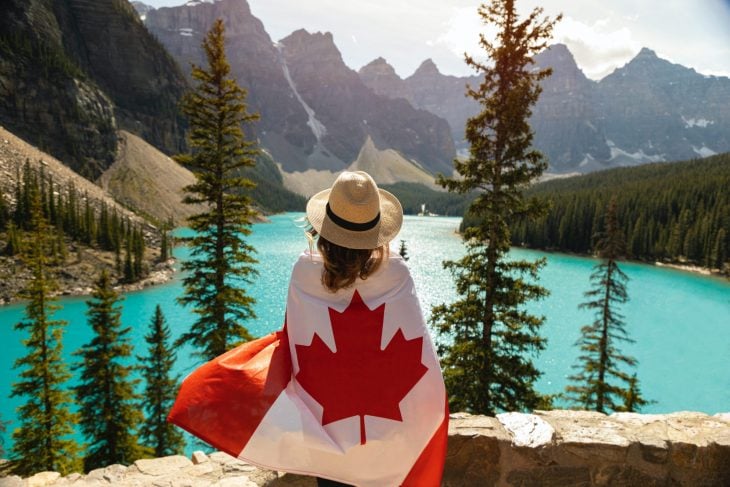 Chica abrazando una bandera de canadá mientras ve un lago