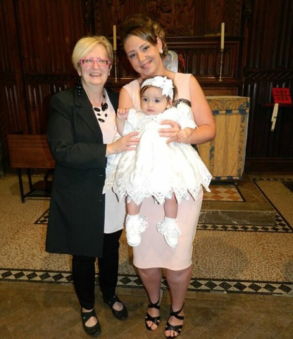 Photograph of an elderly woman next to a girl with a baby in her arms 