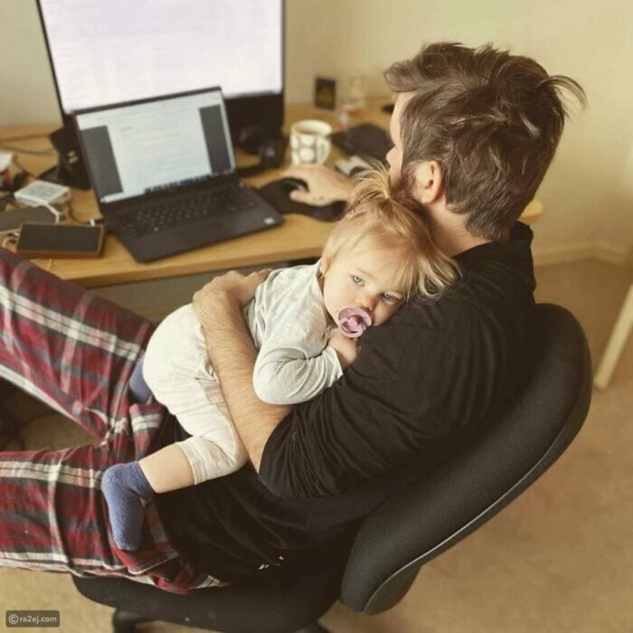 hombre cargando a su hija mientras trabaja en la computadora 
