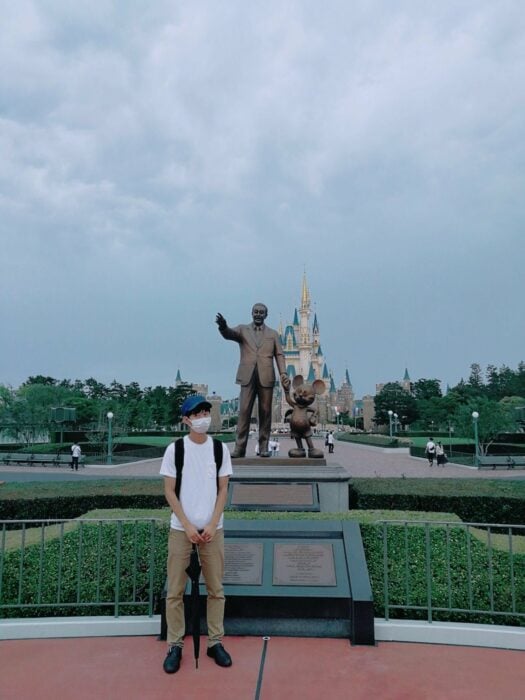chico japonés posando frente a una estatua de Walt Disney 