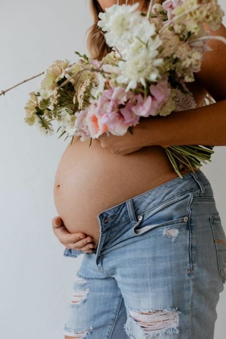 imagen de una chica mostrando su pancita de embarazo con unas flores 