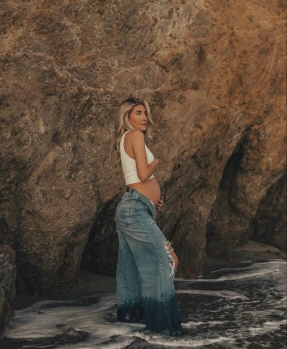 chica embarazada posando en la playa frente a una roca