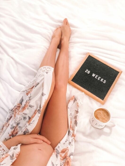 Imagen de una mujer embarazada con un letrero y un café sobre la cama