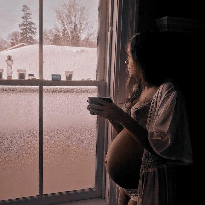 foto de una chica embarazada tomando su café junto a una ventana 