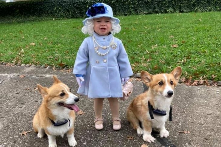 niña disfrazada de la Reina Isabel ll con dos perros a su lado 