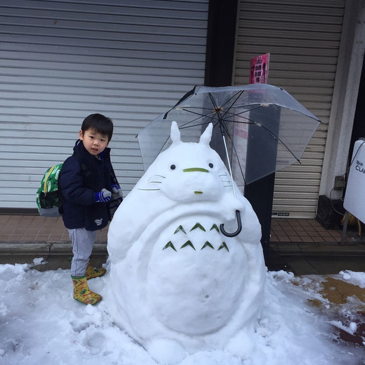 boy standing next to a snow sculpture in the form of the character Totoro