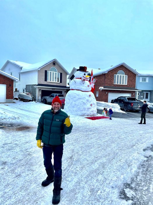 hombre señalando un mono de nieve gigante frente a su casa 