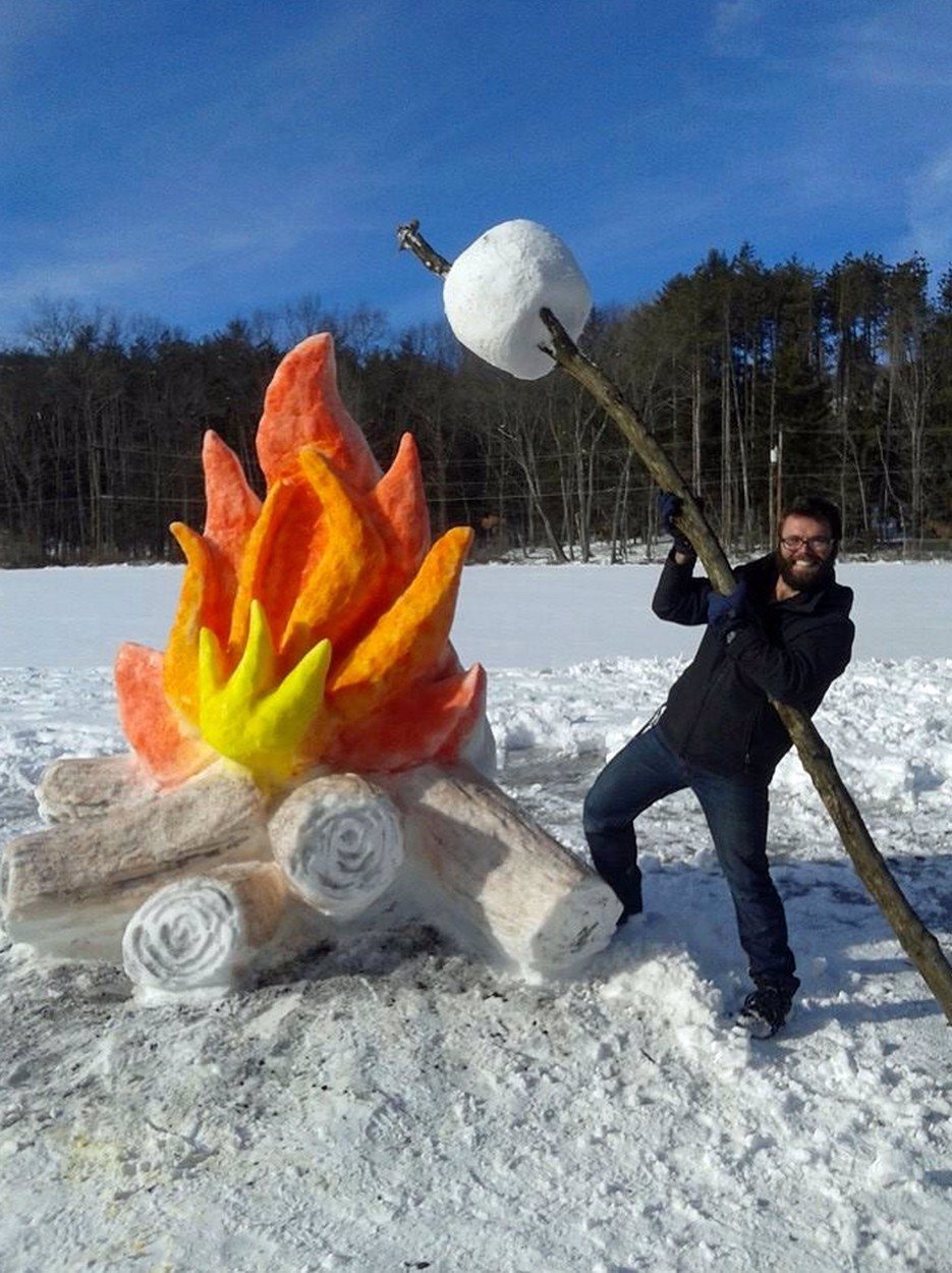 man with a large snow marshmallow at a large campfire created with snow 
