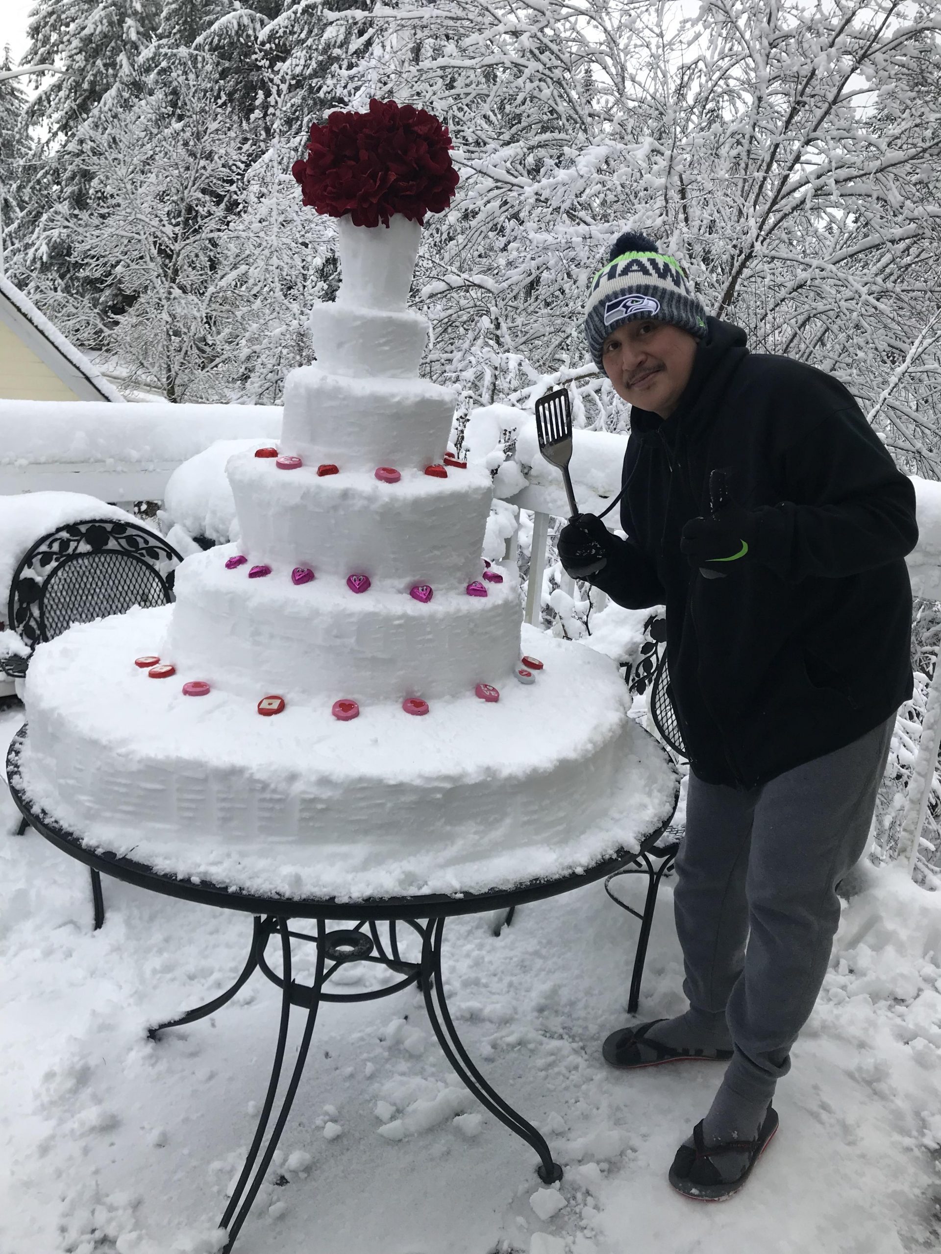 man posing next to a snow sculpture in the form of a giant cake 