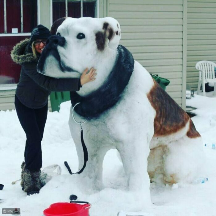 mujer abrazando a una enorme escultura de nieve en forma de perro 