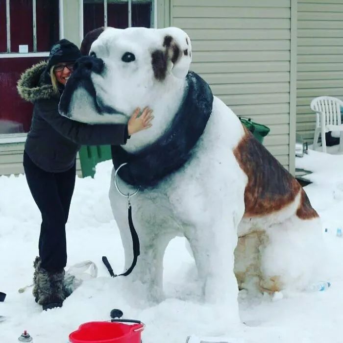 woman hugging a huge snow sculpture in the shape of a dog 