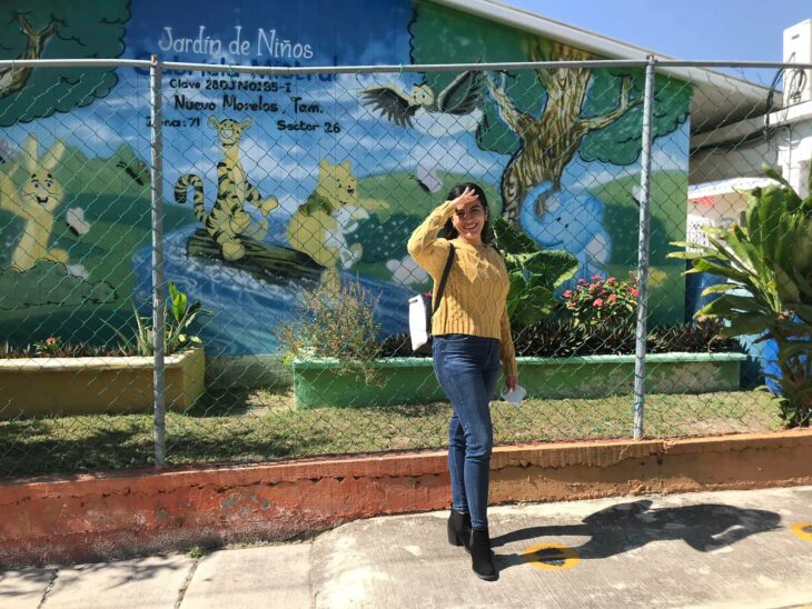 Fotografía de una chica frente a la fachada de un jardín de niños en Tamaulipas 