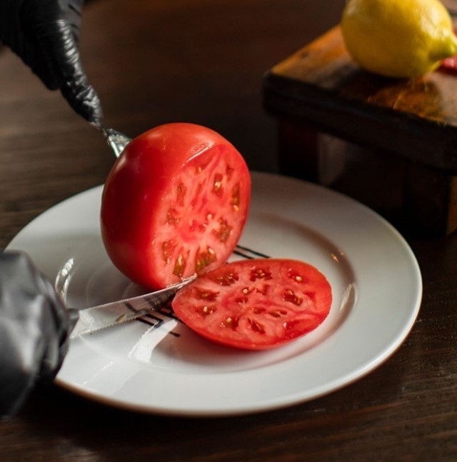 foto de unos cubiertos cortando un jitomate grande en un plato 