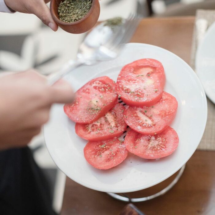 manos de una persona condimentando unas rebanadas de jitomate sobre un plato 