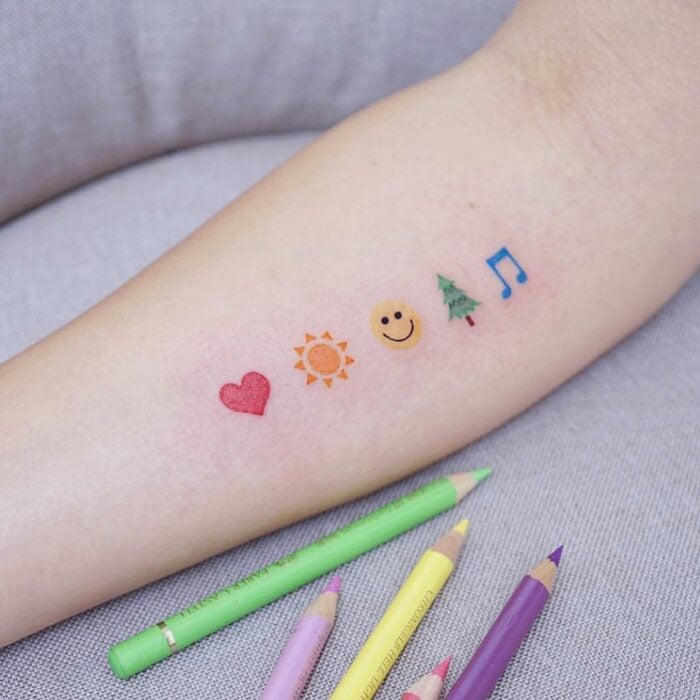 tatuajes de diferentes emojis de colores en el brazo de una persona