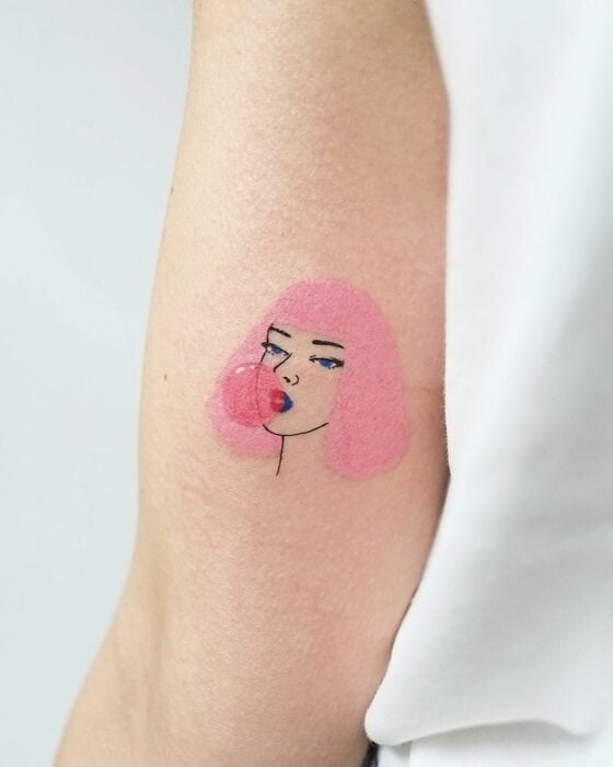 tatuaje de una mujer de pelo rosa con una burbuja de chicle en el brazo de una persona 