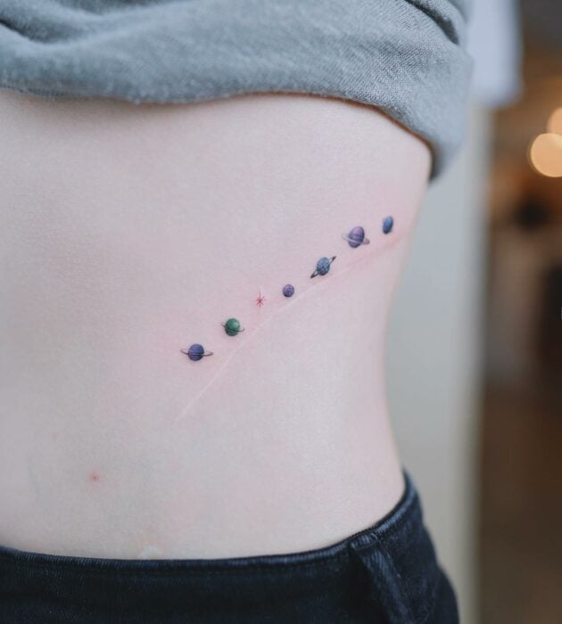 tatuaje de varios planetas de colores en la parte lateral en el cuerpo de una mujer