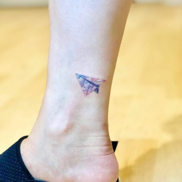 tatuaje de un pequeño avioncito de papel en un tobillo