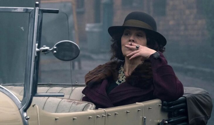Polly Shelby sobre un auto fumando cigarrillo 