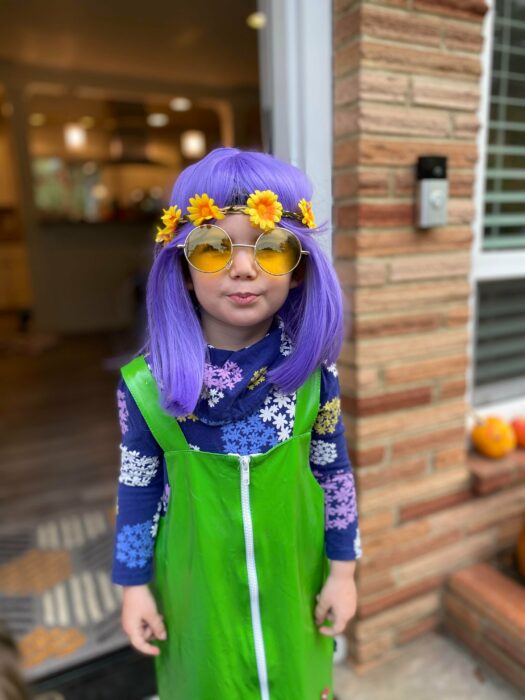 niña con una peluca en color morado y un vestido color verde 