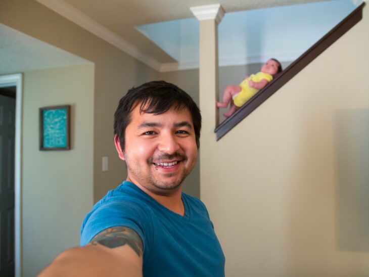 hombre tomando una selfie mientras su bebé está en el pasamanos de la escalera 