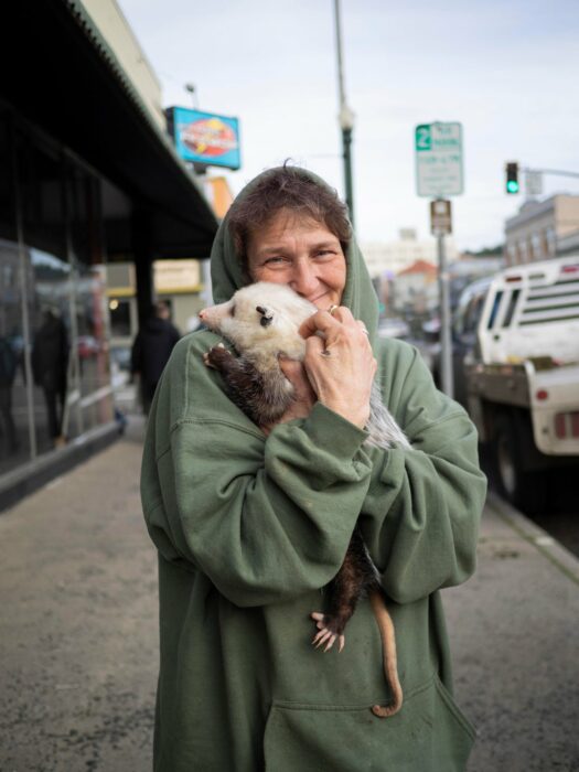 woman holding a possum while hugging her with a smile on her face 