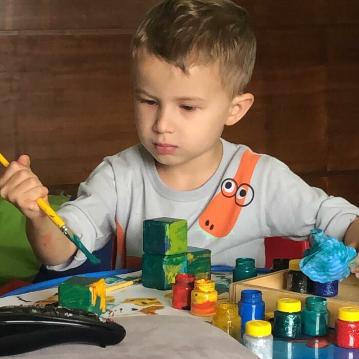 niño sosteniendo un pincel en su mano con algunas pinturas en una mesa 