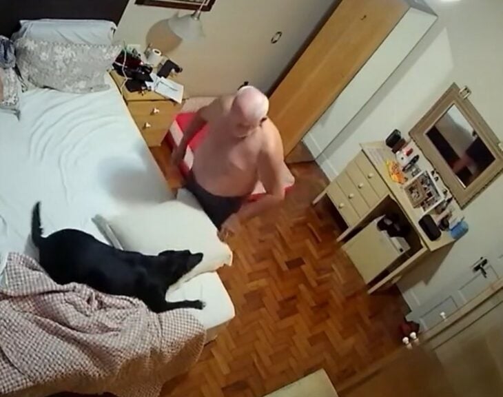 imagen de un hombre parado frente a su cama jugando con su perra 
